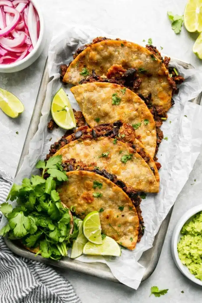 Crispy Black Bean Tacos (Vegetarian, Easily Vegan) 4 Crispy black bean tacos on tray with lime wedges and cilantro