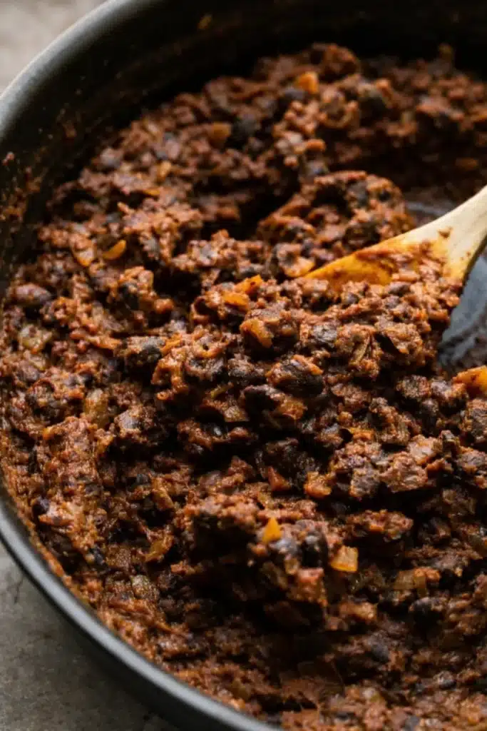 Crispy Black Bean Tacos (Vegetarian, Easily Vegan) 2 Thick black bean taco filling simmering in skillet with wooden spoon
