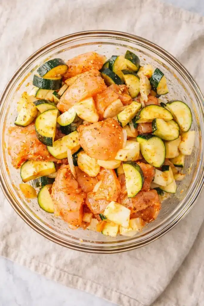 Easy Baked Chicken and Zucchini (Dinner Recipe That’s Fast, Healthy, and One-Dish) 2 Raw chicken and zucchini tossed in paprika marinade in a glass bowl