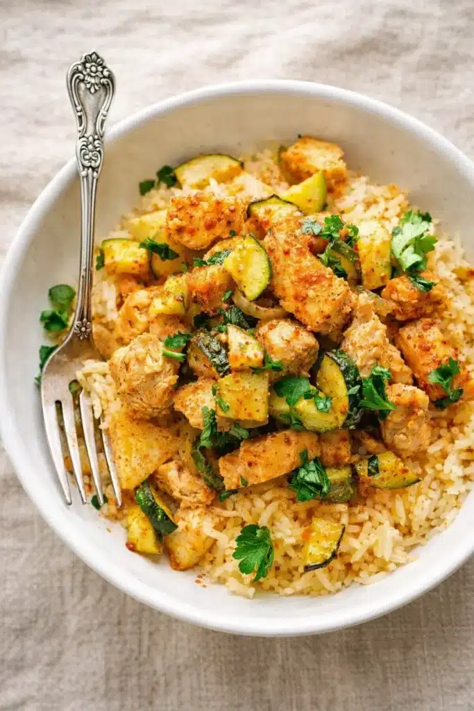 Easy Baked Chicken and Zucchini (Dinner Recipe That’s Fast, Healthy, and One-Dish) 1 Easy baked chicken and zucchini served over rice in a white bowl with fresh herbs