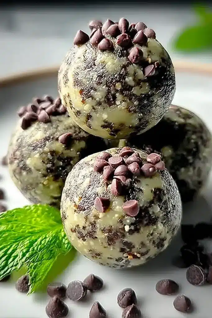 Mint Chocolate Chip Protein Balls 1 Mint chocolate chip protein balls stacked on a plate with chocolate chips and mint leaves