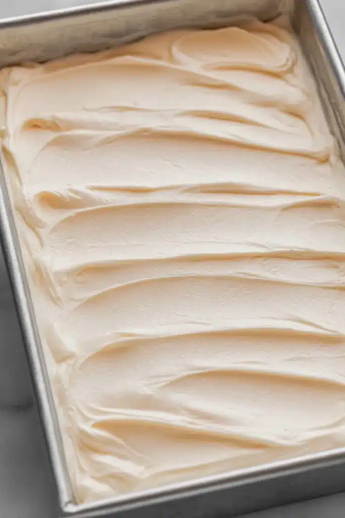 Creamy orange frosting layer spread over orange creamsicle cake in pan