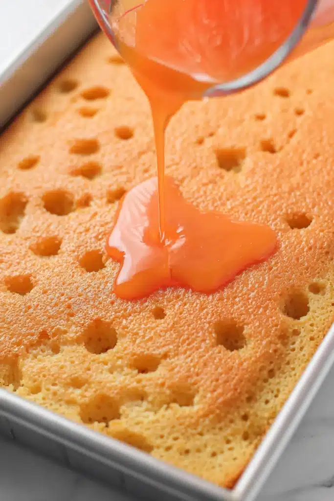 Pouring orange gelatin over poke cake in baking pan