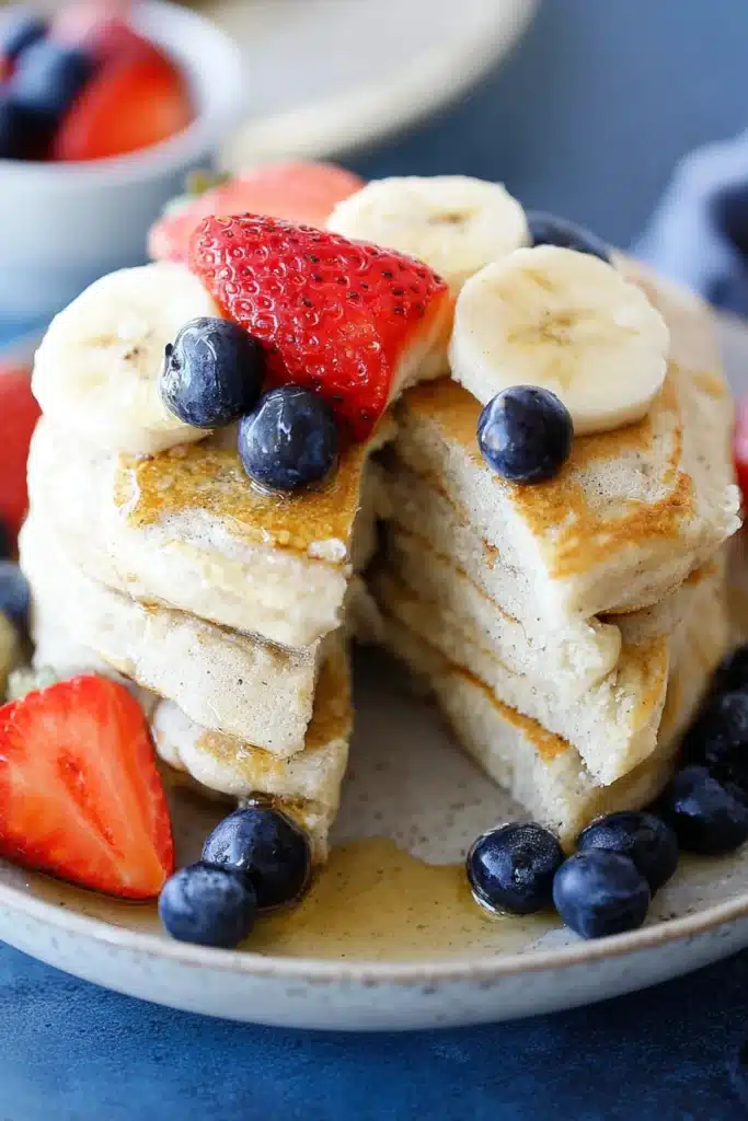 Fluffy protein pancakes with banana, strawberries, blueberries, and maple syrup