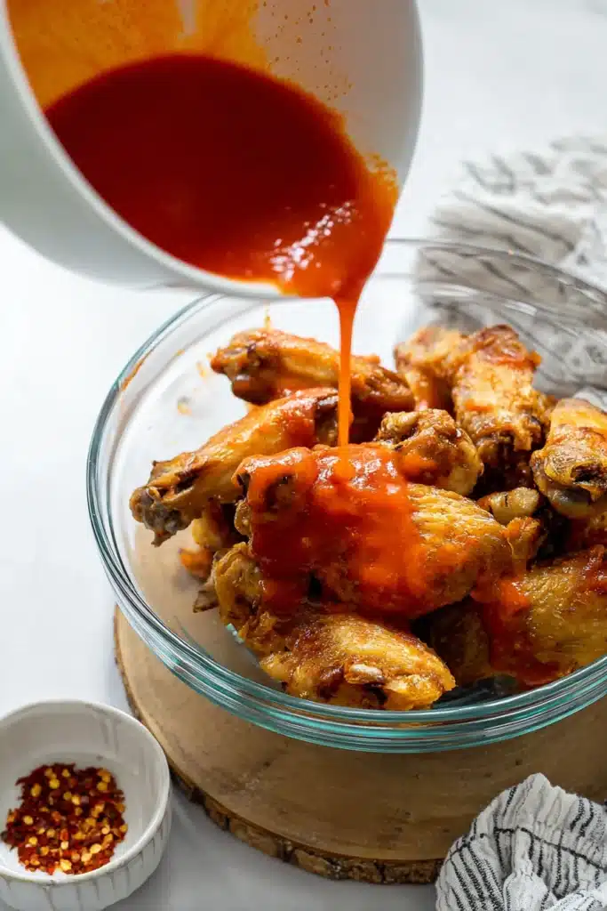 Air Fryer Buffalo Chicken Wings Recipe – Crispy, Spicy, and Ready Fast 3 Pouring buffalo sauce over crispy air fryer chicken wings in a glass bowl