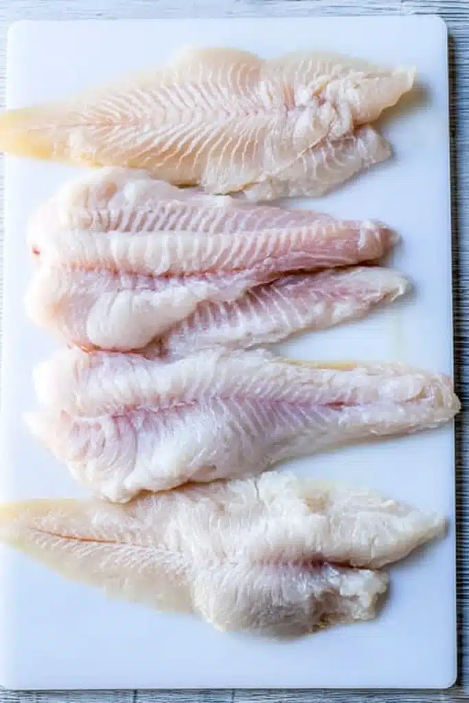 Raw catfish fillets on a white cutting board ready for air fryer recipe