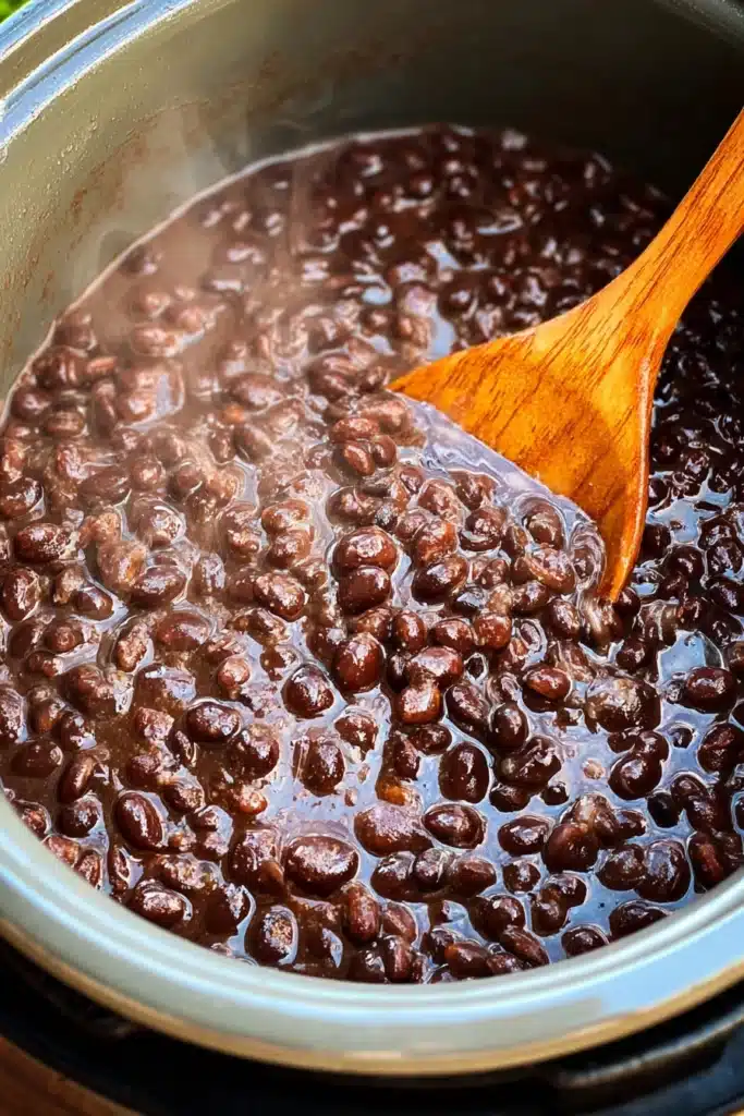 Instant Pot Black Bean Soup (Easy, Hearty & Flavorful) 2 Instant Pot black bean soup simmering in a pot with a wooden spoon