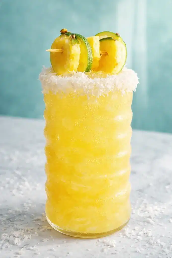 Non alcoholic piña colada punch in tall glass with coconut rim and pineapple garnish