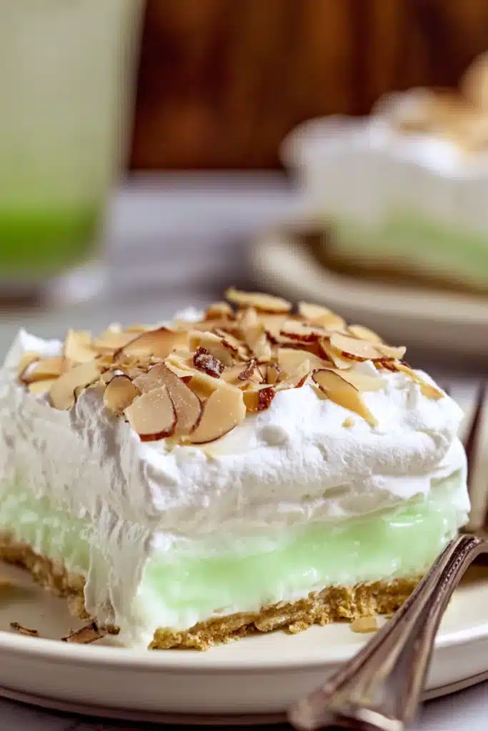 Pistachio Lush Recipe That’s Creamy, Easy, and Crowd Pleasing 1 Slice of pistachio lush dessert with whipped topping and toasted almonds on white plate