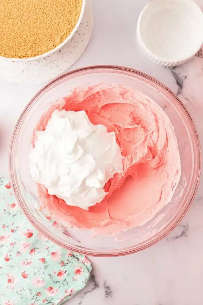 Mixing Strawberry Jello Cream Pie filling with whipped topping in a glass bowl