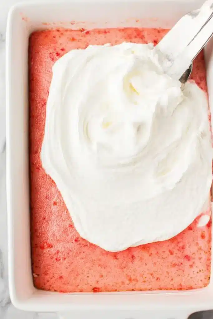 Strawberry Jello Poke Cake | Easy, Moist, and Refreshing Dessert 3 Spreading whipped topping on strawberry Jello poke cake