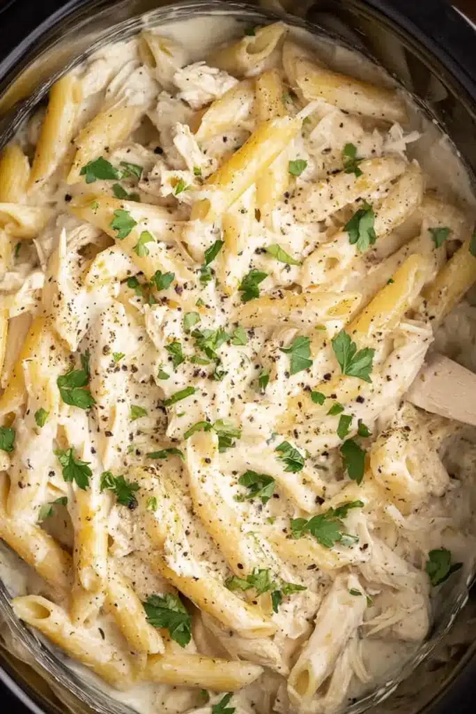 The BEST Chicken Alfredo Slow Cooker Recipe 2 The BEST Chicken Alfredo cooking in a pot with creamy sauce and penne pasta