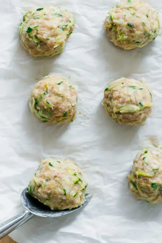 Raw Whole30 chicken meatballs with zucchini on parchment paper before air frying