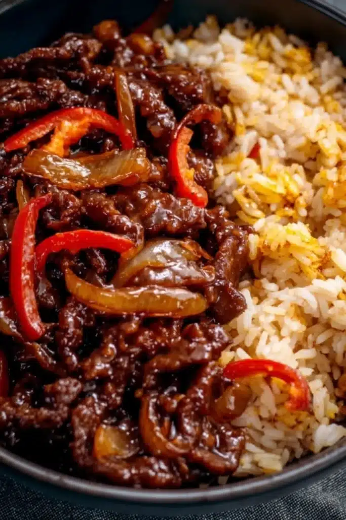 Crispy Chilli Beef Recipe 2 Crispy chilli beef with fried rice in dark bowl, sweet-spicy glaze and red chillies