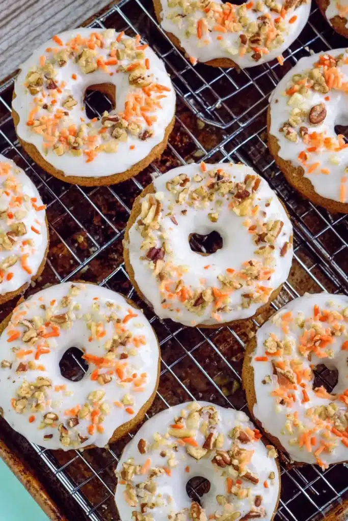 Carrot Cake Donuts with cream cheese frosting, walnuts, and orange sprinkles cooling on a wire rack