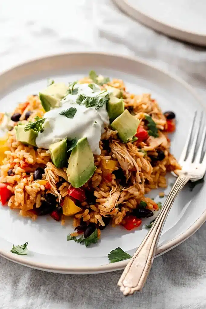 Easy chicken burrito casserole with avocado, black beans, and sour cream on ceramic plate