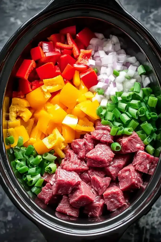 Slow Cooker Pepper Steak ingredients with raw beef and bell peppers in crockpot