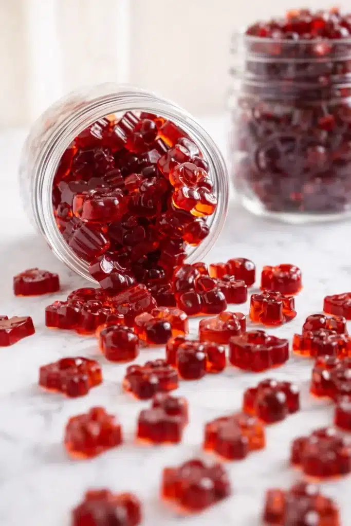 Homemade tart cherry gummies spilling from a glass jar on a light surface
