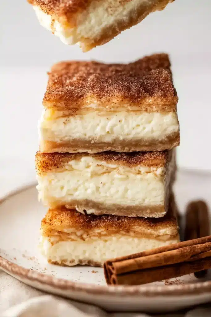 Churro Cheesecake Bars 1 Churro cheesecake bars stacked with creamy layers and cinnamon sugar topping