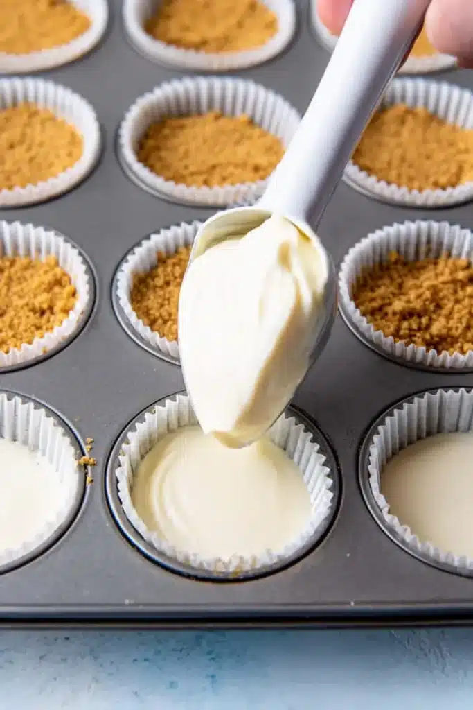 Mini Cheesecake Cups 3 Mini Cheesecake Cups batter being scooped into muffin liners over graham cracker crust