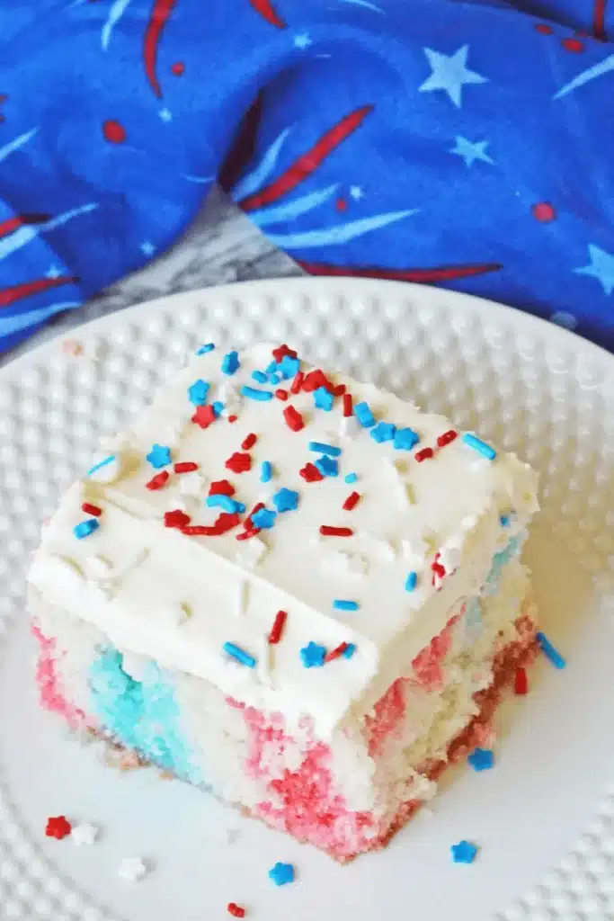 Red white and blue poke cake slice with creamy frosting and festive sprinkles