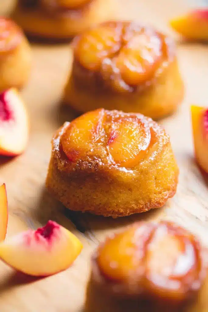 Peach upside down mini cakes with caramelized peaches on top on a rustic surface