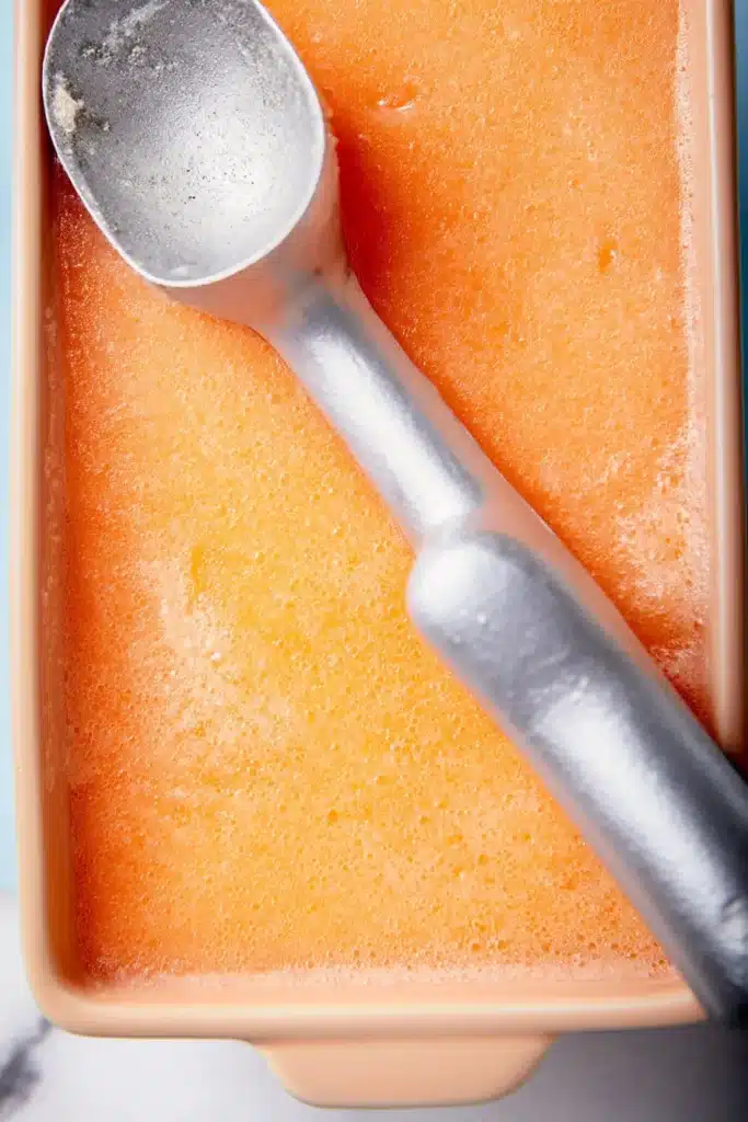 Peach Sorbet frozen in a container with a scoop ready to serve